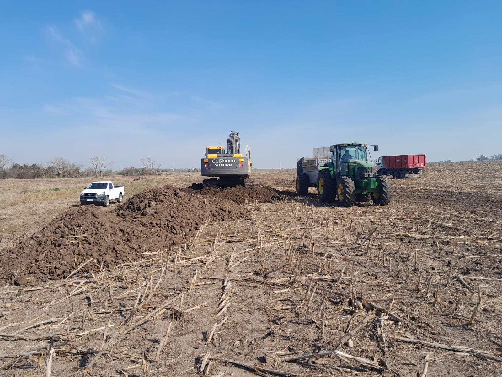 Maquinaria pesada trabajando en la remoción de tierra en un campo agrícola como parte de obras de remediación ambiental.